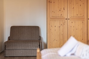 Una habitación con una silla tapizada de color marrón, un armario de madera y una cama con almohada blanca.