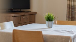 Una habitación con una televisión sobre un mueble de madera, un cuadro en la pared, una pequeña planta en maceta sobre una mesa y una cortina a cuadros.