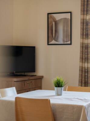 A room with a television on a wooden cabinet, a framed picture on the wall, a small potted plant on a table, and a plaid curtain.