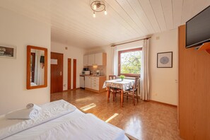 Una habitación con cama, una mesa de comedor con sillas, una zona de cocina y un televisor instalado en la pared.