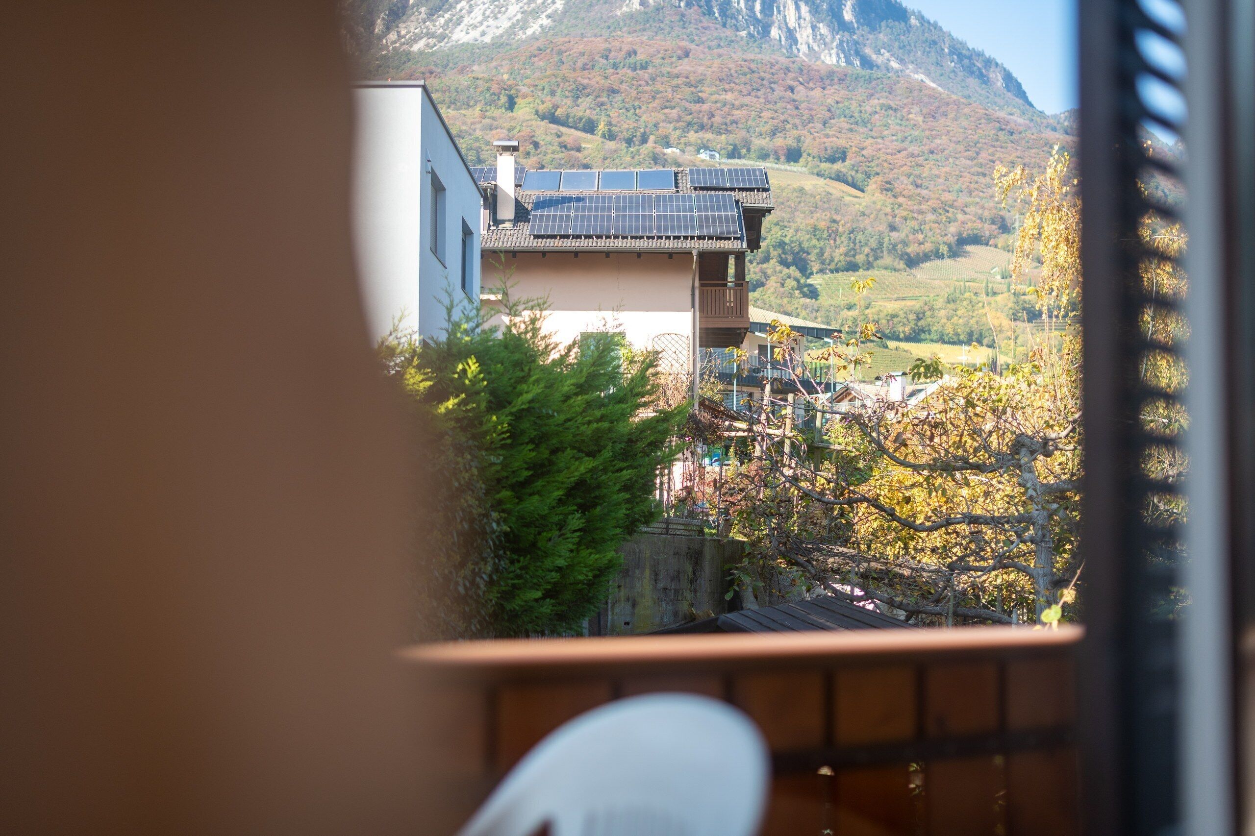 A traditional building with a sloped roof and solar panels, surrounded by trees and a mountainous backdrop.