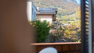 A traditional building with a sloped roof and solar panels, surrounded by trees and a mountainous backdrop.