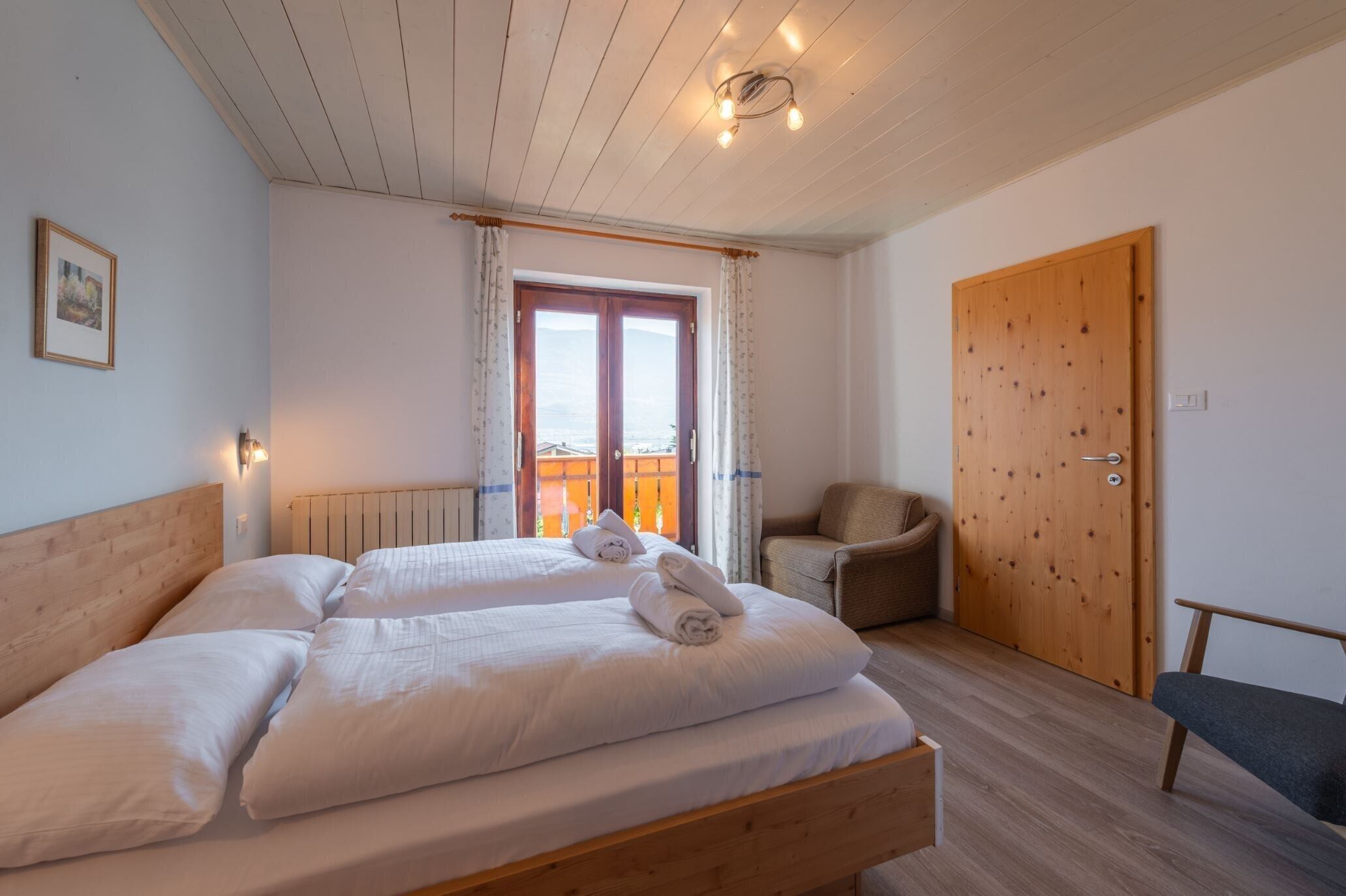Une chambre à coucher avec un lit en bois, une chaise, une porte en bois et une fenêtre avec des rideaux.