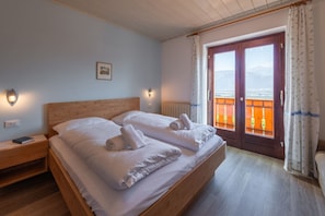 Ein Doppelbett mit weißen Leinen und Handtüchern, ein Nachttisch mit einem Buch, eine Wandleuchte und ein Fenster mit Blick auf einen Balkon.