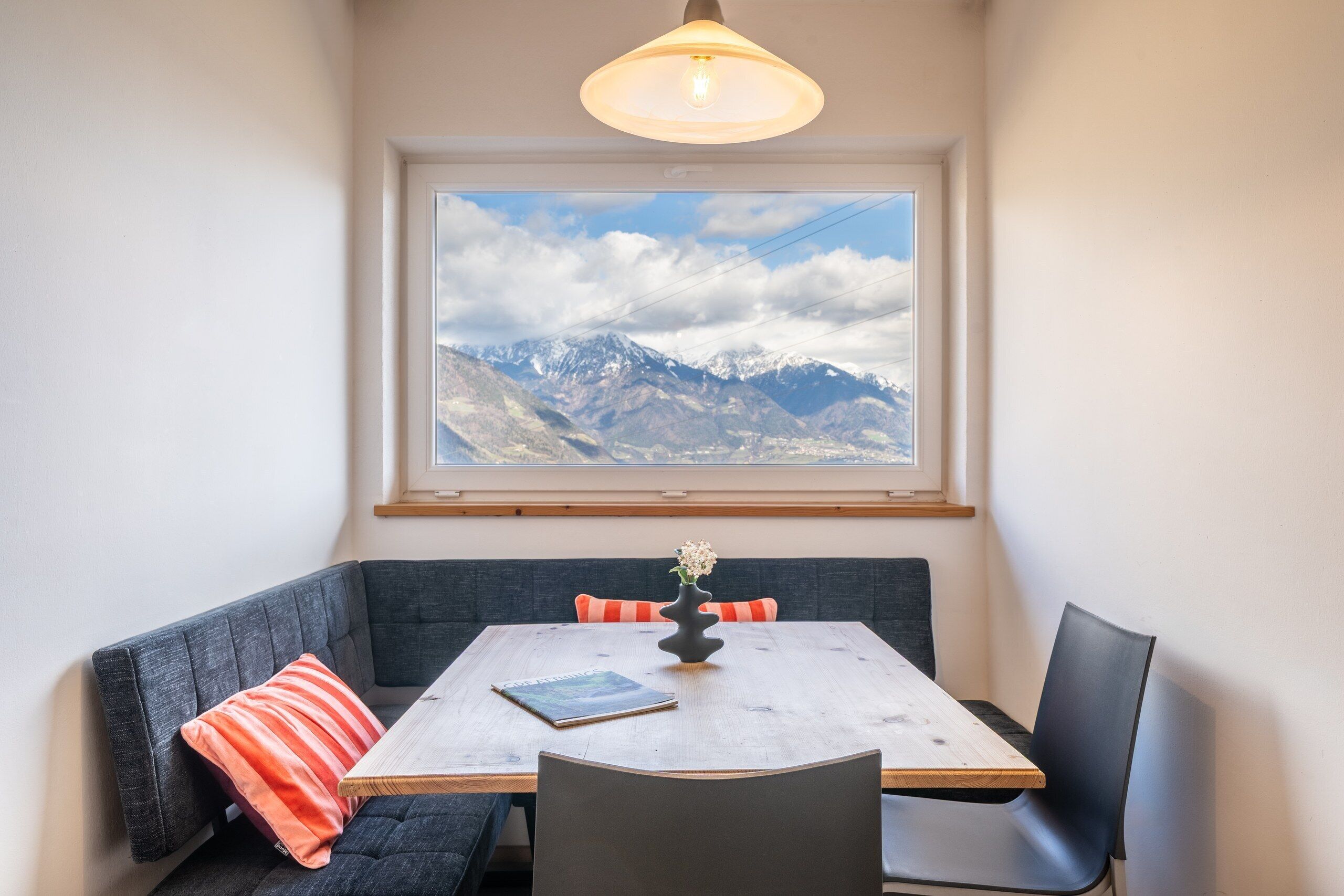 Ein Essbereich mit Tisch, Stühlen und Blick auf Berge durch ein Fenster.