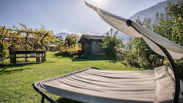 Un espacio al aire libre con césped, una hamaca, un banco de madera y una pequeña construcción de madera.