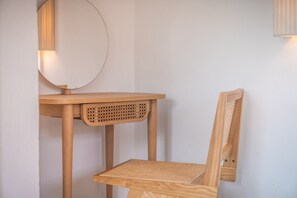 Ein Holzstuhl mit gewebter Sitzfläche und Rückenlehne, ein passender Holztisch mit rundem Spiegel und eine wandmontierte Leuchte.