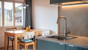 Une cuisine moderne avec une table à manger en bois, des chaises, un évier encastré et une fenêtre avec des rideaux.