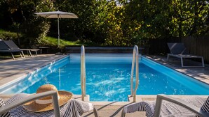 Une piscine équipée de deux échelles, de chaises longues et d’un parasol.