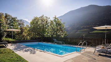 Ein Pool mit Blick auf Berge, umgeben von einem Holzzaun und von Bäumen beschattet.