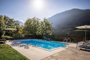 Une piscine avec vue sur les montagnes, entourée d’une clôture en bois et ombragée par des arbres.