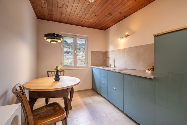Une cuisine avec un plafond en bois, une table de salle à manger ronde entourée de chaises, une fenêtre donnant sur les montagnes et un évier avec un robinet.