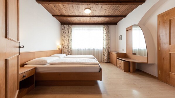 Un dormitorio con techo de madera, una cama con dos almohadas, una mesita de noche, un espejo y una ventana con cortinas.