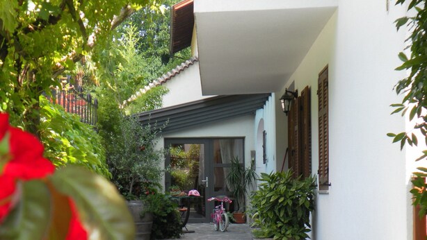 A courtyard with a bicycle, potted plants, and a white building with wooden shutters. - 724C Residence Hofgarten (Caldaro sulla strada del vino)