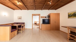A room with a wooden ceiling, a dining area with a table and chairs, a television on a wooden cabinet, and a doorway leading to another room. - 724C Residence Hofgarten (Caldaro sulla strada del vino)