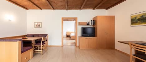 A room with a wooden ceiling, a dining area with a table and chairs, a television on a wooden cabinet, and a doorway leading to another room.