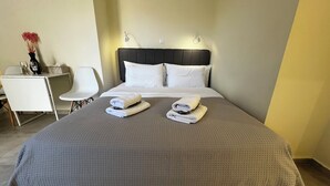 Ein ordentlich bezogenes Bett mit zwei gefalteten Handtüchern, ein Nachttisch mit einer Vase und Weingläsern sowie ein Sessel in einem Hotelzimmer.