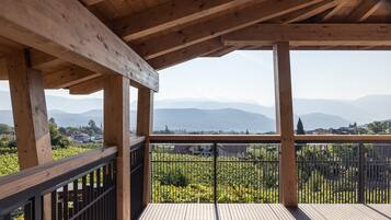 Un balcon en bois offrant une vue sur un vignoble et des montagnes lointaines.