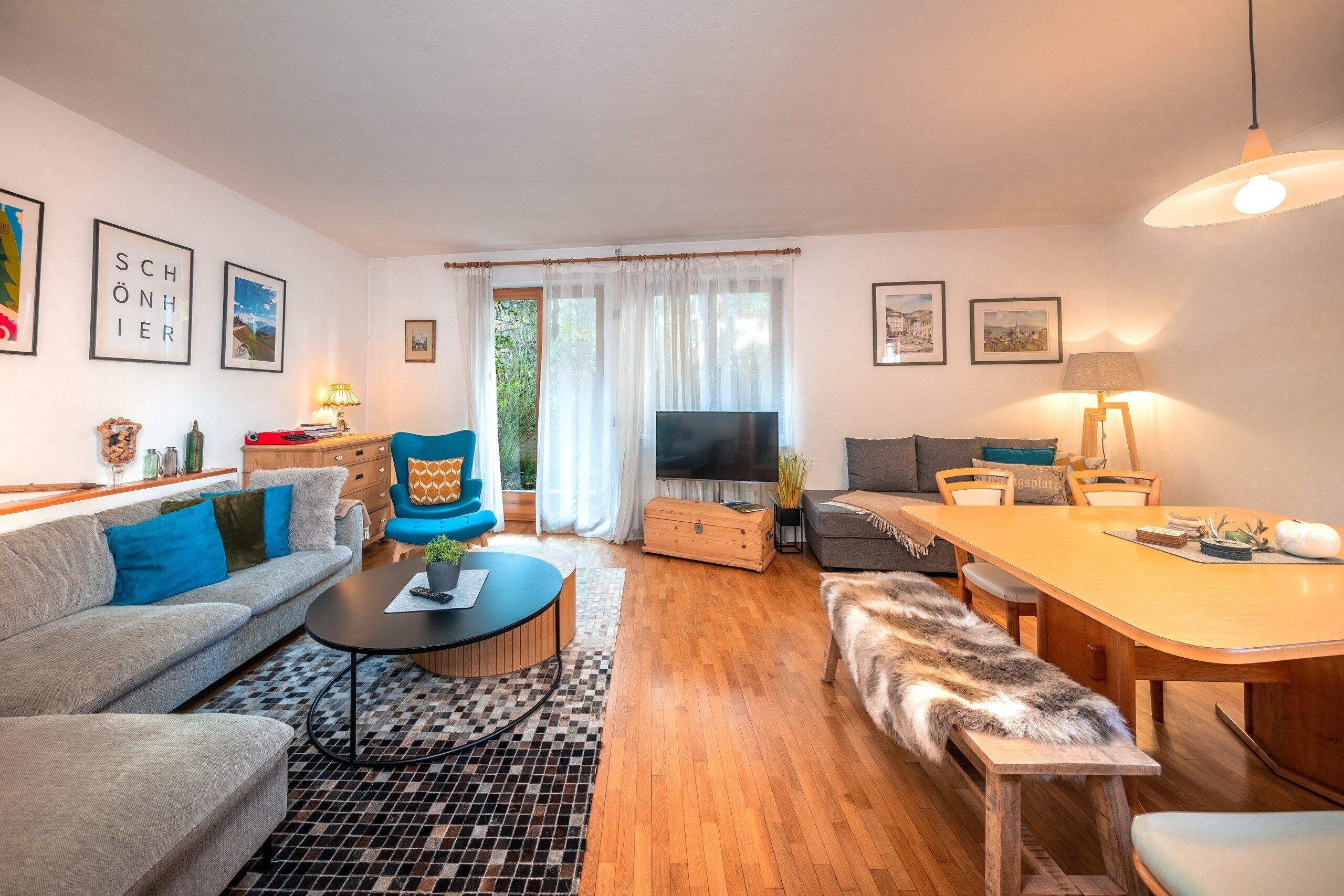 A modern living room with a sofa, a blue armchair, a coffee table, a television, and a dining area with a table and chairs.