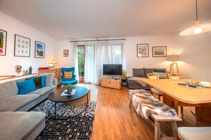 Ein modernes Wohnzimmer mit einer Couch, einem blauen Sessel, einem Couchtisch, einem Fernseher und einem Essbereich mit Tisch und Stühlen.
