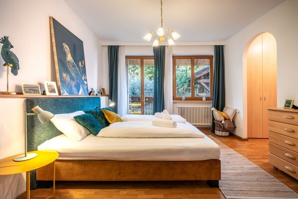 A bedroom with a bed, bedside tables, a dresser, a window with curtains, and a painting on the wall.
