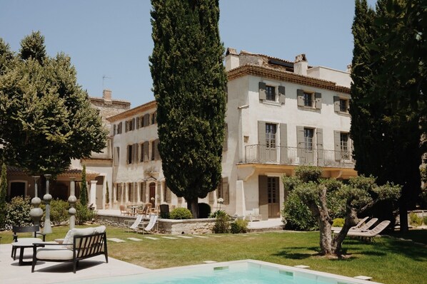 A large building with a swimming pool, outdoor seating, and tall trees.