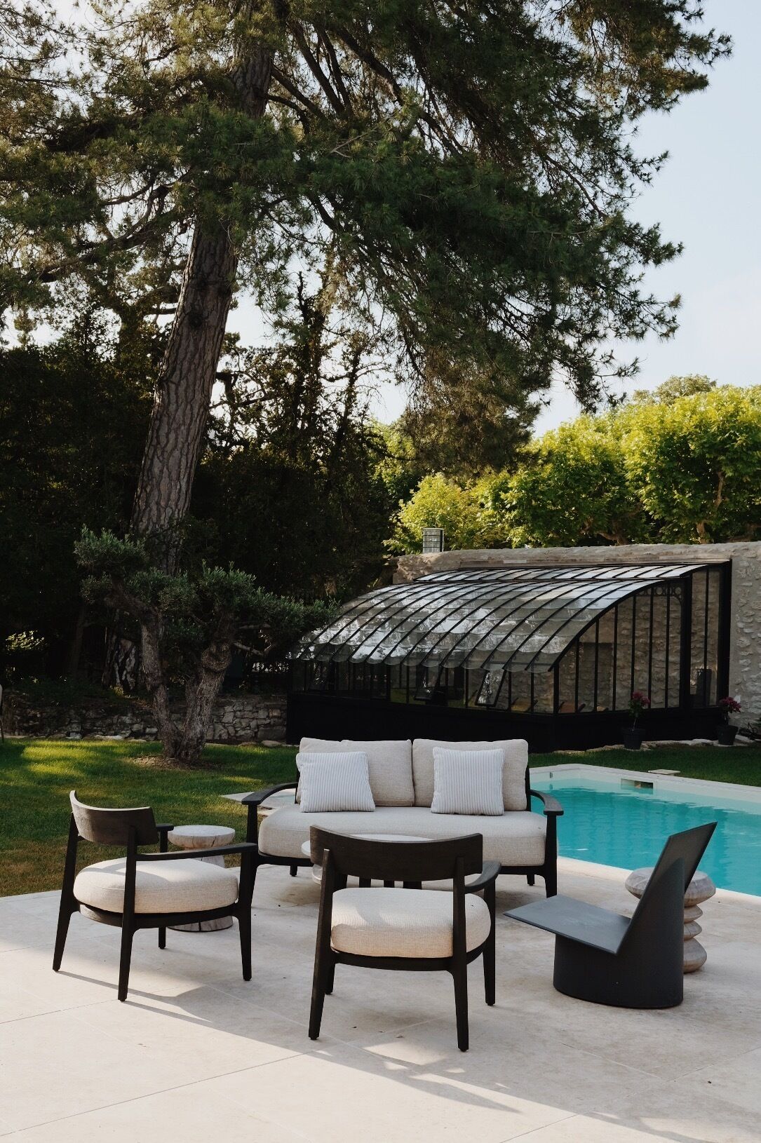 Un espace extérieur aménagé avec des sièges, une piscine, le tout entouré d’arbres et d’une structure en forme de serre.