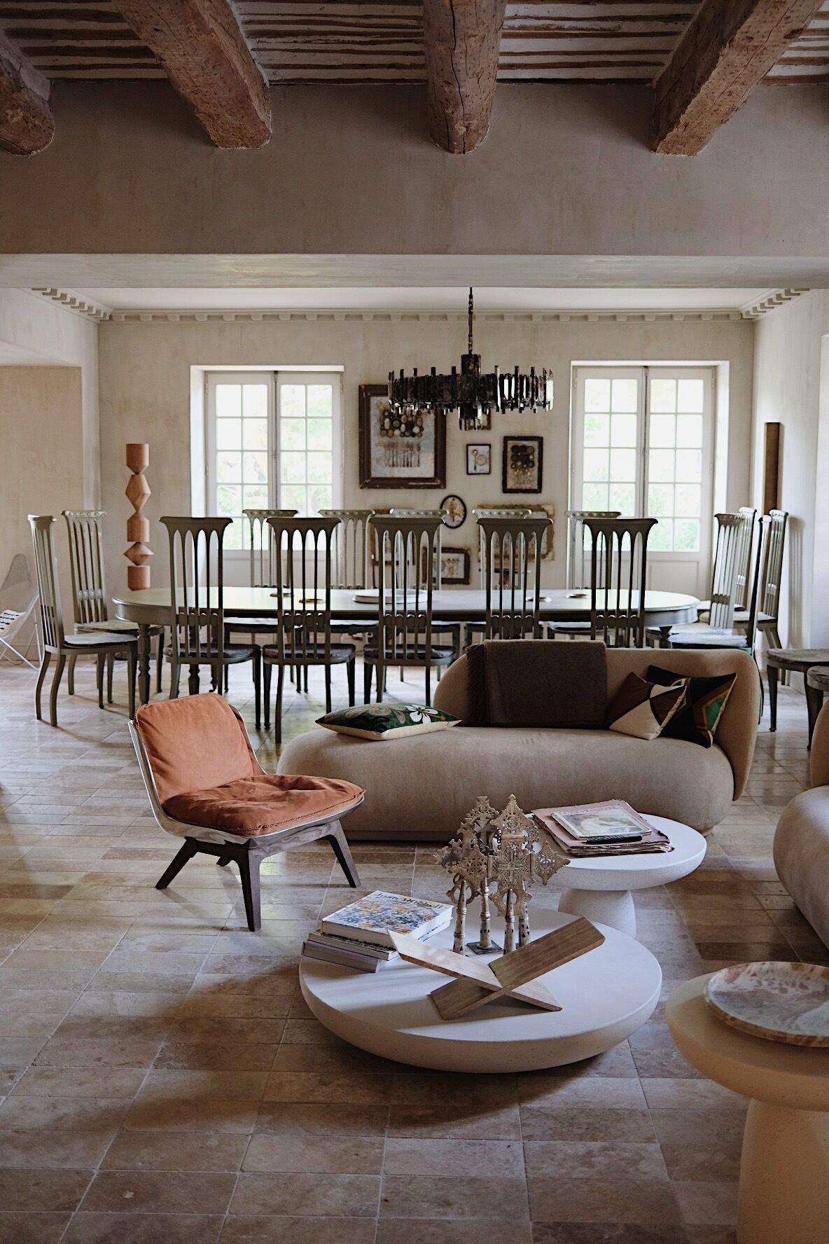 A spacious living room with a high ceiling, a dining area with a chandelier, and a sofa with cushions.