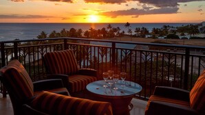 A balcony with wicker furniture and a table set for drinks, overlooking a beach and ocean at sunset. - 3br + 2br on the Same Floor - Sleeps 13! Amazing for Families (Kapolei)