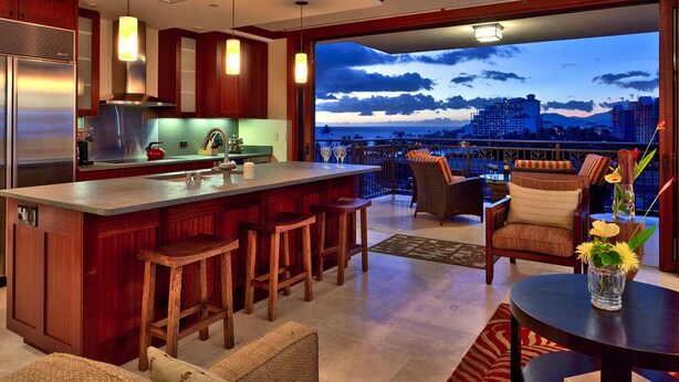 A modern kitchen with a large island, bar stools, and a view of the city at dusk. - 3br + 2br on the Same Floor - Sleeps 13! Amazing for Families (Kapolei)