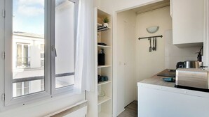 A compact kitchen with white cabinets, a small countertop, and a window with curtains.