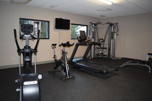 Ein Fitnessstudio mit verschiedenen Trainingsgeräten, darunter Laufbänder, ein Crosstrainer und ein Kraftgerät.