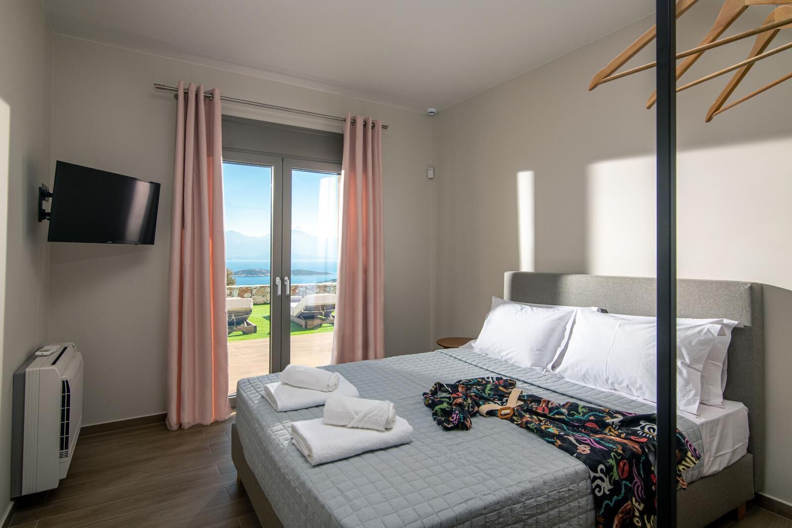 A bedroom with a bed, a flat-screen TV, a heater, and a balcony with curtains.