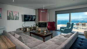 Una sala de estar moderna con un sofá grande, un televisor de pantalla plana, una chimenea y vista al mar.