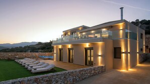 Una casa moderna con un muro de piedra, una piscina y sillones de descanso.