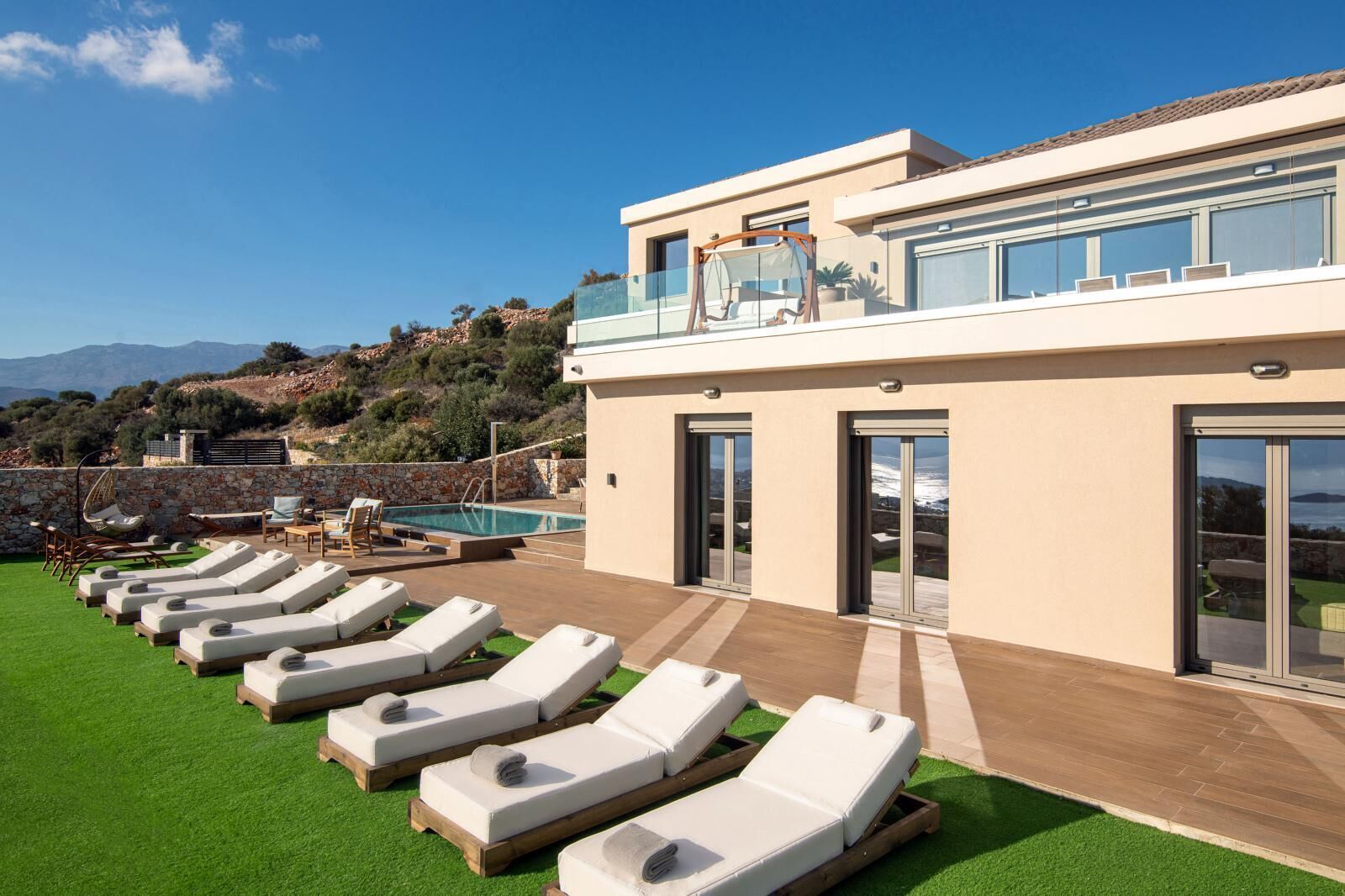 A modern villa with a pool, sun loungers, and a view of the mountains.