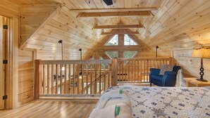 A wooden cabin with a loft bedroom, a wooden staircase, and a view of the outdoors.
