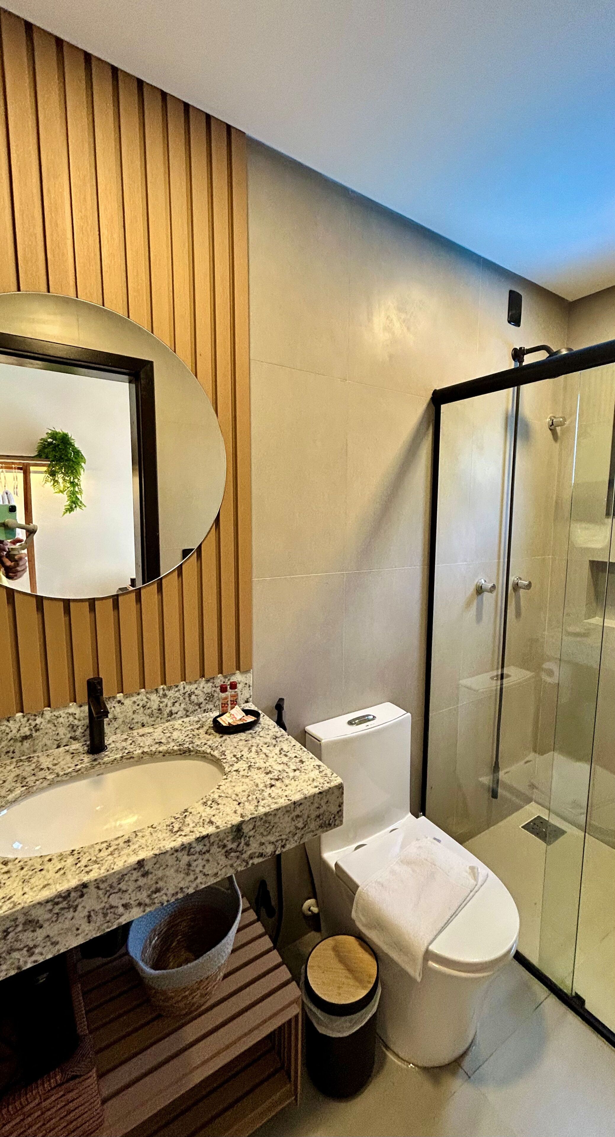 Une salle de bain moderne avec un comptoir en granit, des toilettes, une douche en verre et un mur recouvert de panneaux en bois.