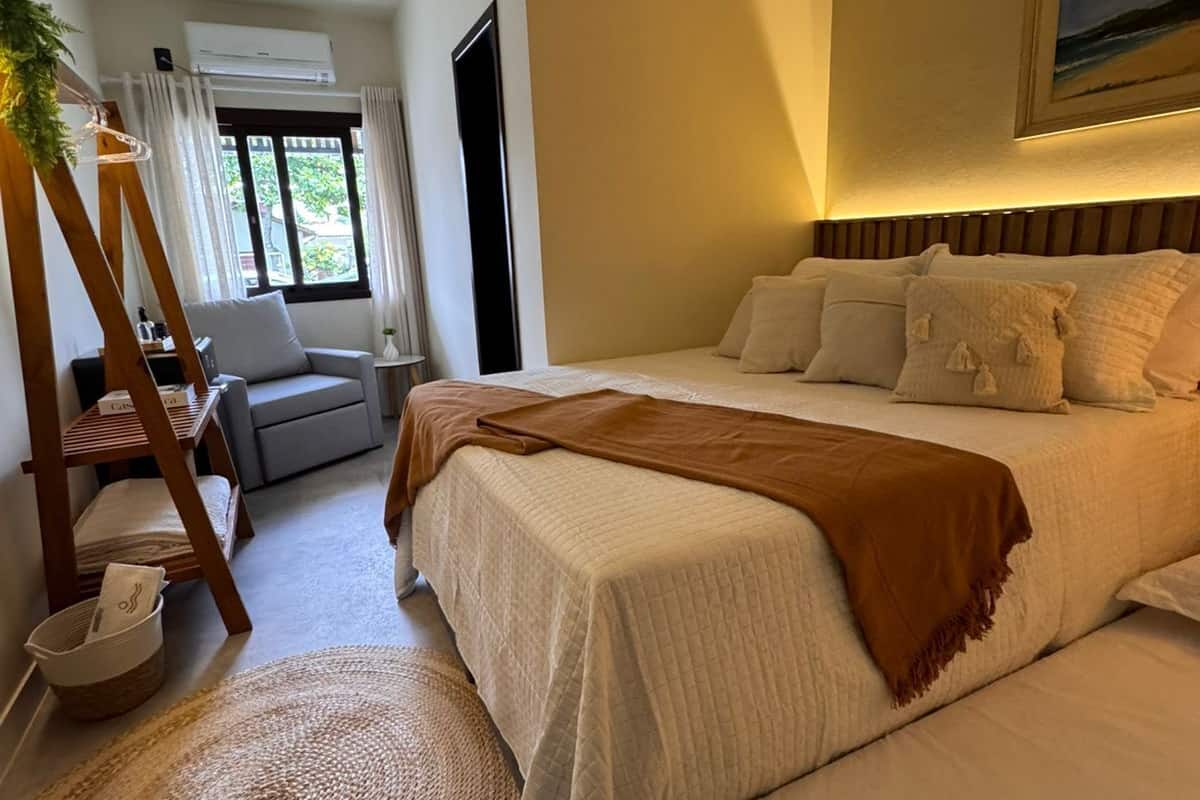 A bedroom with a large bed, a small sofa, a wooden ladder, and a woven rug.