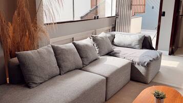 A modern living room with a grey sectional sofa, a wooden coffee table, and a large window with a view of a building.
