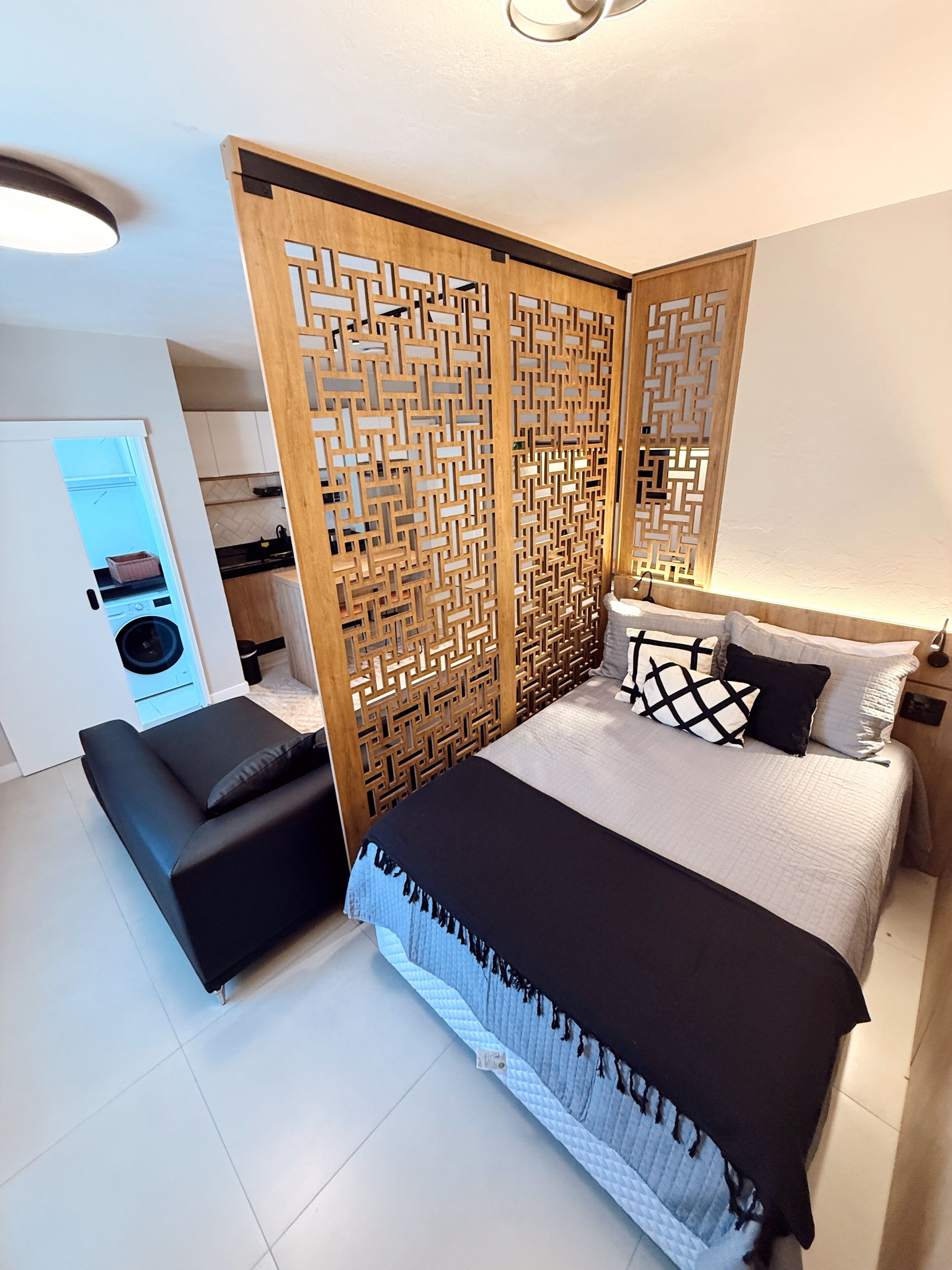 A modern bedroom with a large bed, a black sofa, and a wooden partition with a geometric pattern.