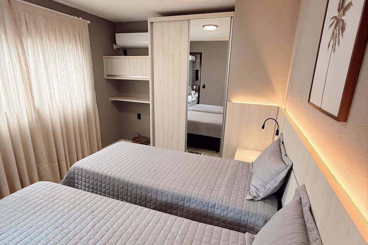 A hotel room with two beds, a mirror, a ceiling light, and a framed picture on the wall.