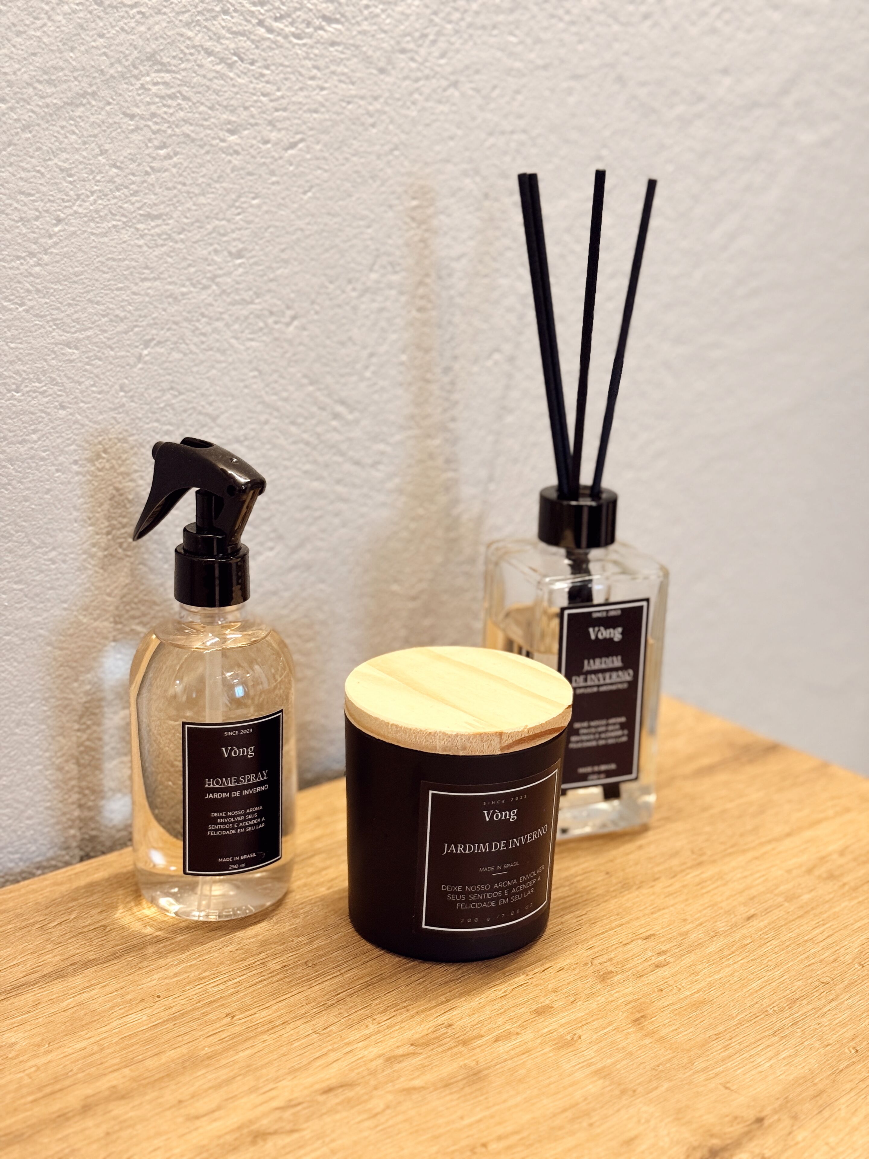 Tres botellas de Vang Home Spray sobre una superficie de madera frente a una pared con textura.