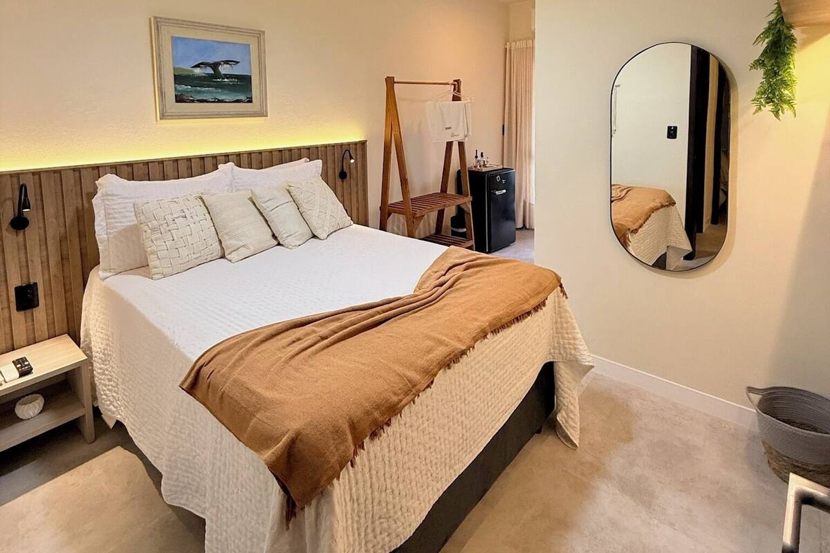 A bedroom with a bed, a ceiling fan, a bedside table, a nightstand, a mirror, and a wall-mounted shelf.