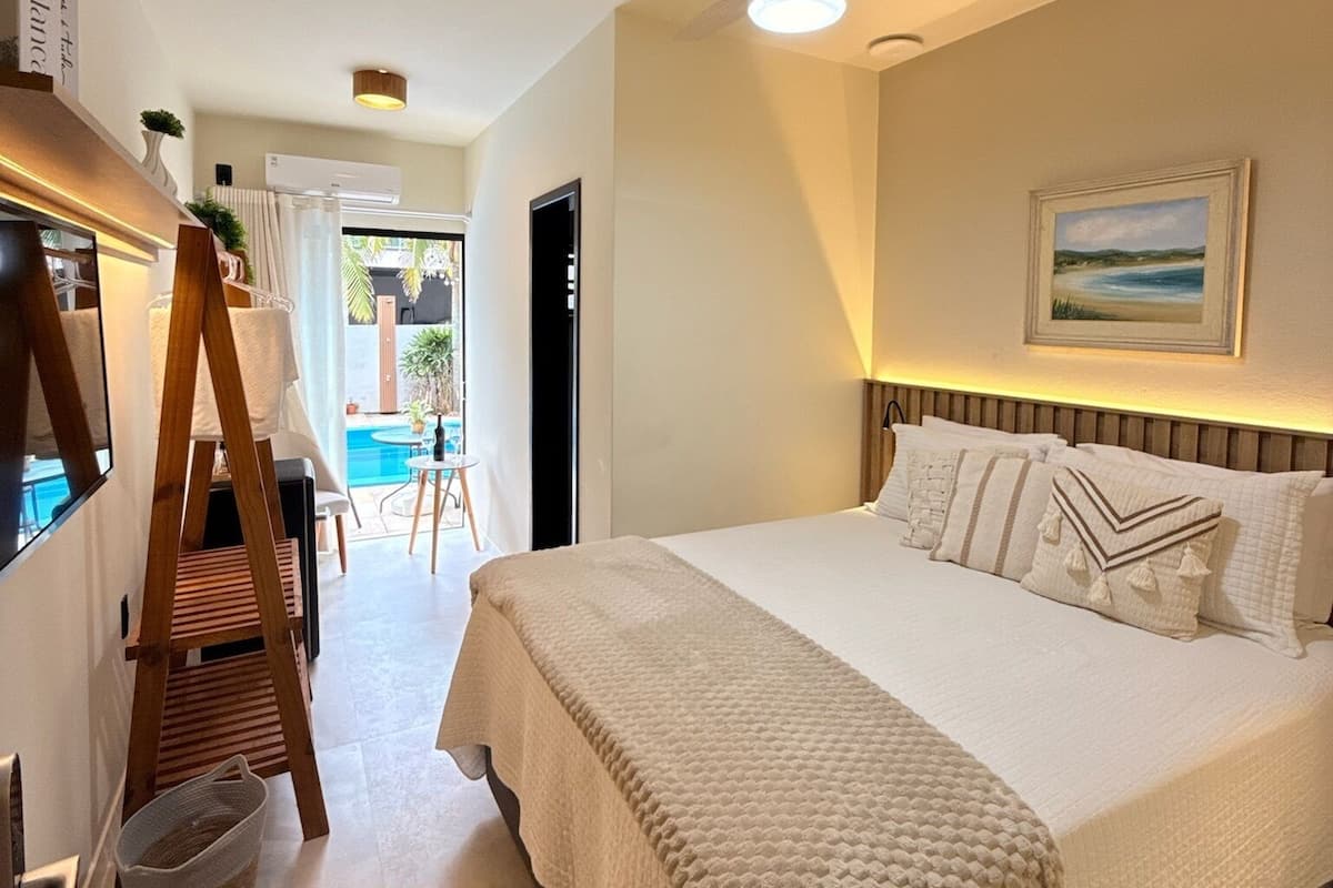 A bedroom with a bed, a ceiling fan, a painting, and a view of a pool.
