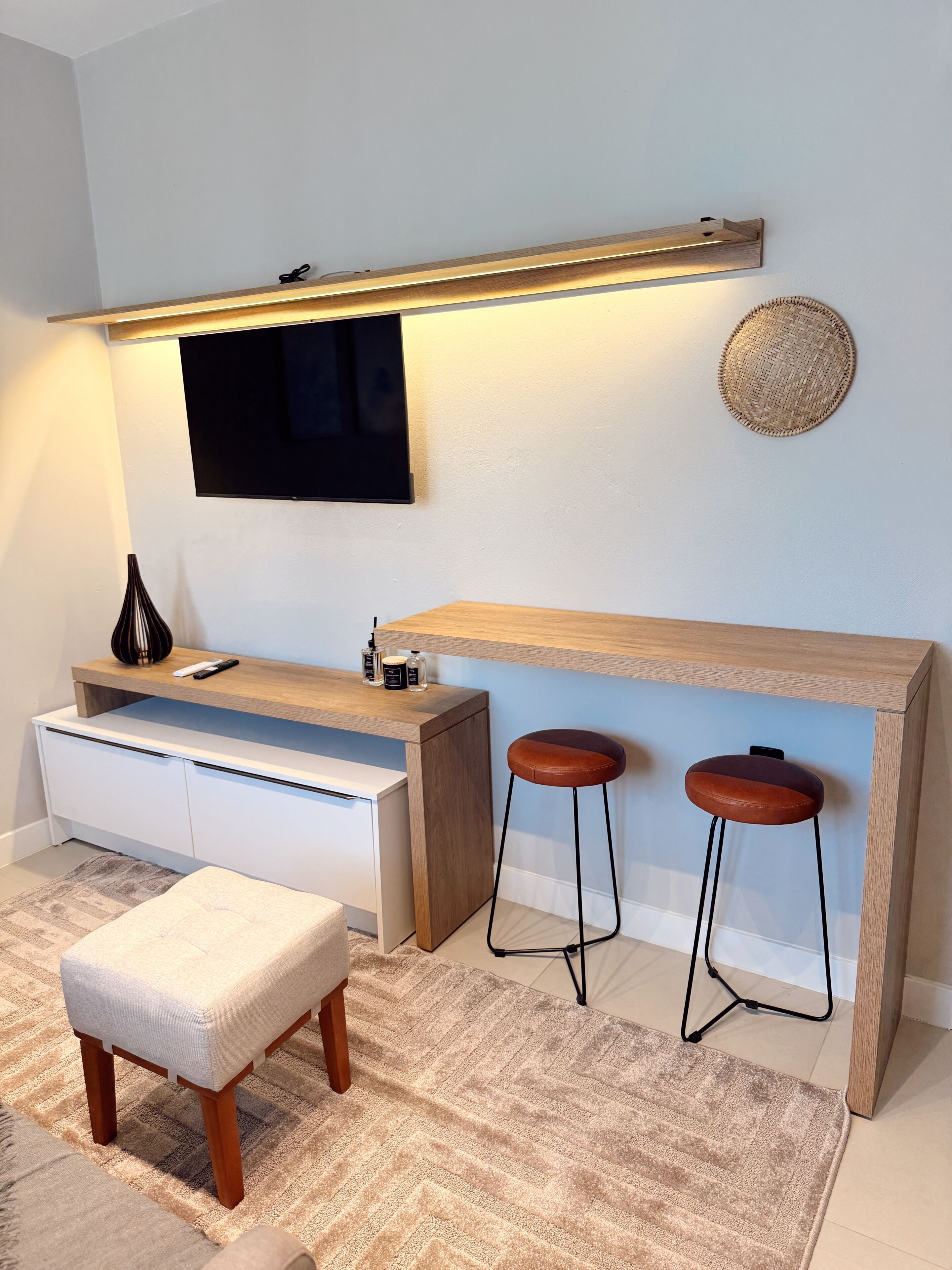 Una sala de estar moderna con un televisor montado en la pared, un mueble bajo para televisión de madera, dos taburetes de bar y un banco.