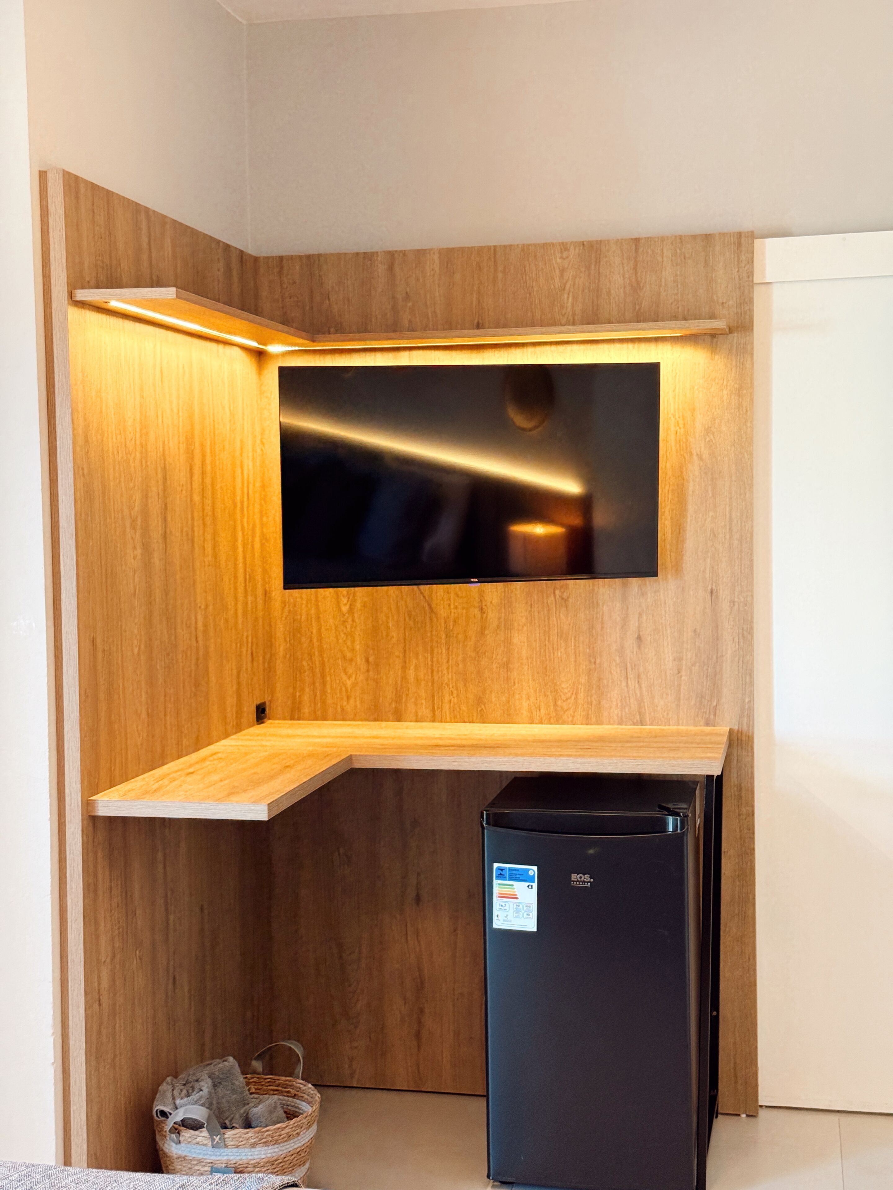 A corner kitchenette with a built-in TV, a black refrigerator, and a wooden shelf.