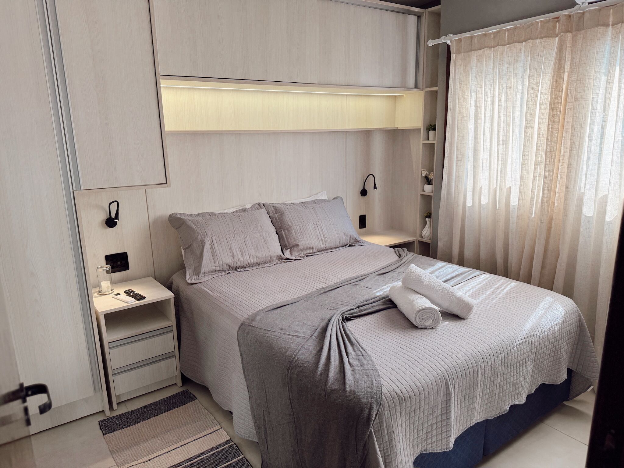 A modern bedroom with a bed, bedside tables, a nightstand, a lamp, and a window with curtains.