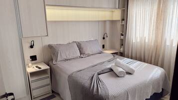 A modern bedroom with a bed, bedside tables, a nightstand, a lamp, and a window with curtains.