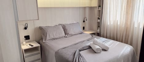 A modern bedroom with a bed, bedside tables, a nightstand, a lamp, and a window with curtains.